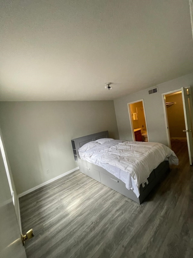 bedroom with a walk in closet, visible vents, baseboards, and wood finished floors