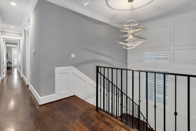 hall with crown molding, dark wood finished floors, a decorative wall, an inviting chandelier, and an upstairs landing