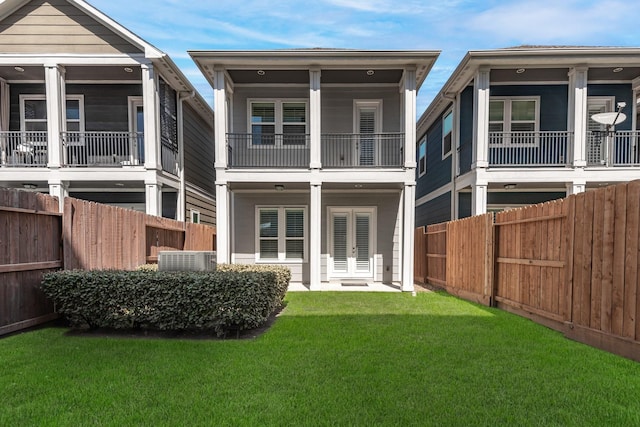 rear view of house with a yard, french doors, a fenced backyard, and a balcony