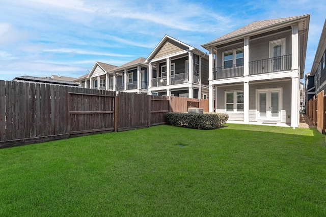 rear view of house with a balcony, a yard, a fenced backyard, and french doors