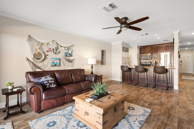 living room with ornamental molding, wood-type flooring, visible vents, and baseboards