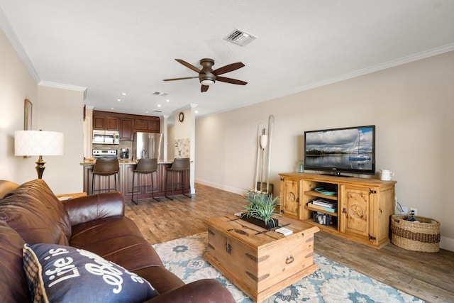 living area with ornamental molding, visible vents, ceiling fan, and light wood finished floors