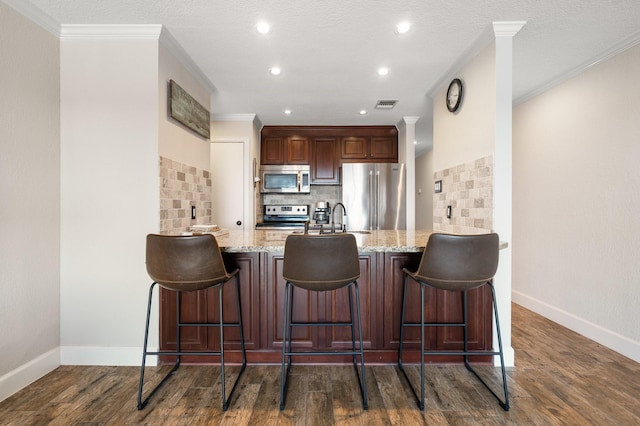 kitchen with dark wood-type flooring, a peninsula, light stone countertops, stainless steel appliances, and crown molding