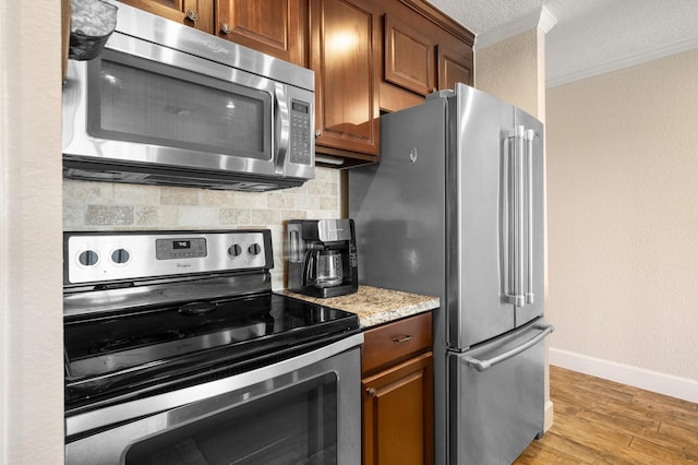 kitchen featuring decorative backsplash, appliances with stainless steel finishes, ornamental molding, light wood-type flooring, and baseboards