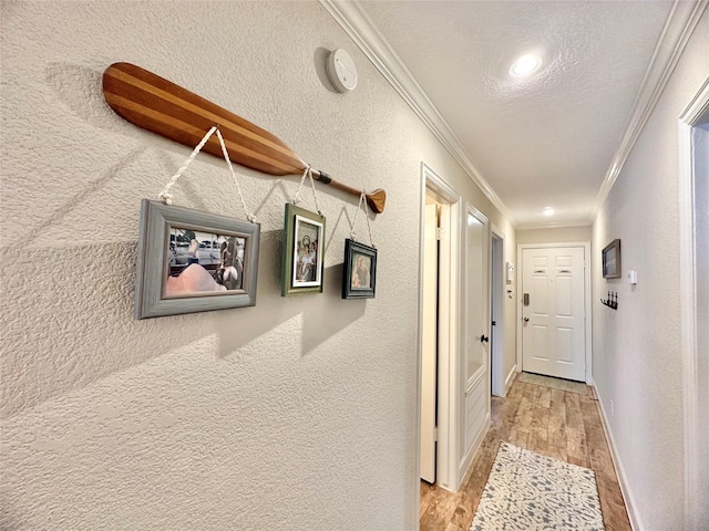 hallway with a textured ceiling, a textured wall, baseboards, ornamental molding, and light wood-type flooring