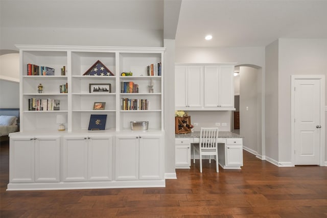 unfurnished office with baseboards, arched walkways, dark wood-style flooring, built in desk, and recessed lighting