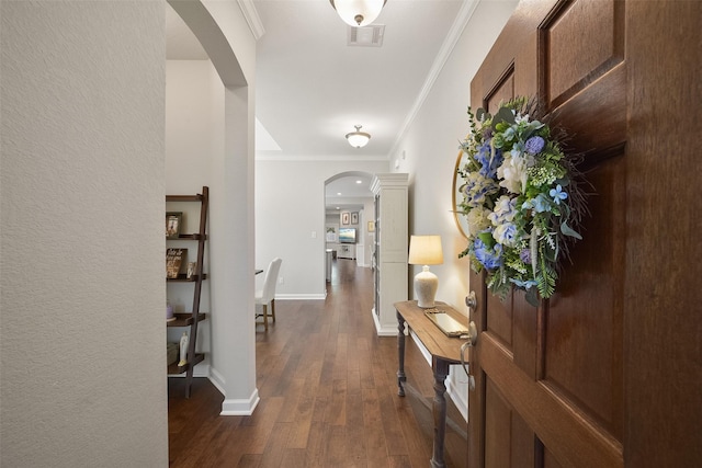 hallway with dark wood-style floors, arched walkways, visible vents, ornamental molding, and baseboards