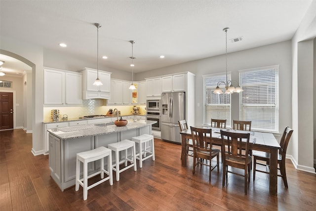 kitchen with arched walkways, stainless steel appliances, visible vents, a kitchen island with sink, and a sink