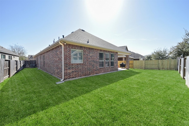 back of property with a shingled roof, brick siding, a yard, and a fenced backyard