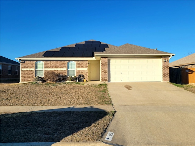 ranch-style house featuring driveway, fence, a garage, brick siding, and solar panels