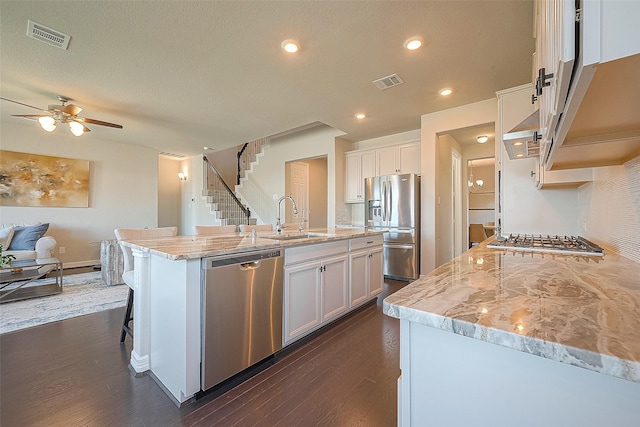 kitchen featuring white cabinets, light stone countertops, stainless steel appliances, and a sink