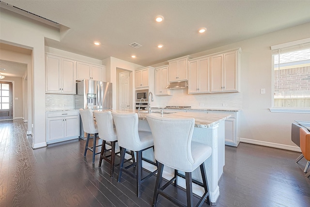 kitchen featuring visible vents, under cabinet range hood, a kitchen bar, appliances with stainless steel finishes, and a sink