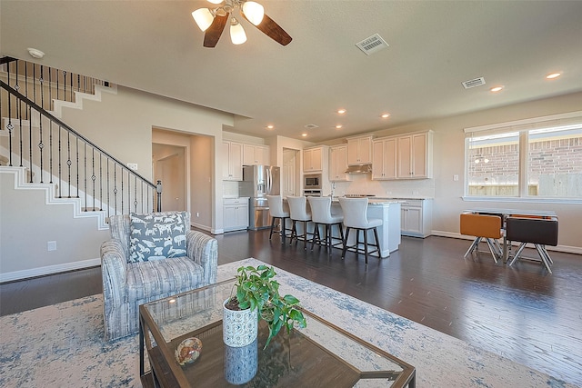 living room with dark wood-style floors, visible vents, stairs, and baseboards