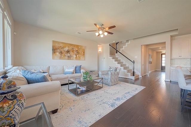 living room featuring visible vents, baseboards, stairs, dark wood-style floors, and a ceiling fan