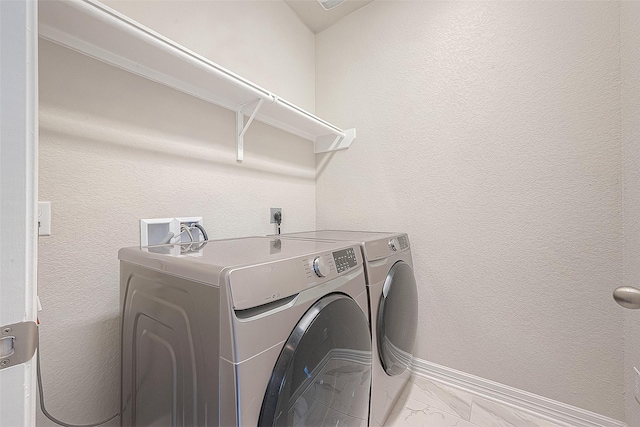 clothes washing area with baseboards, laundry area, washer and dryer, a textured wall, and marble finish floor