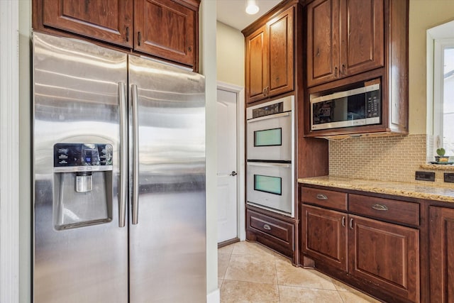 kitchen with light tile patterned floors, appliances with stainless steel finishes, light stone counters, and backsplash