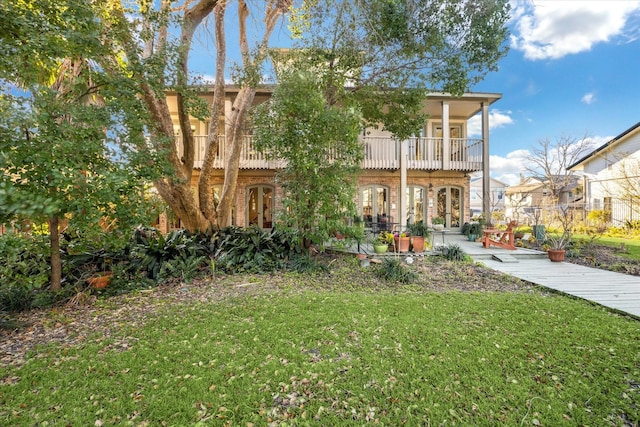 view of front of property with french doors, brick siding, a balcony, and a front lawn