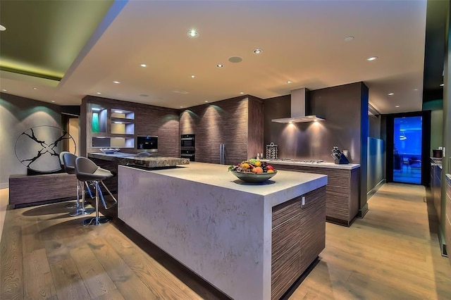 kitchen featuring light wood-style flooring, recessed lighting, light countertops, wall chimney range hood, and modern cabinets