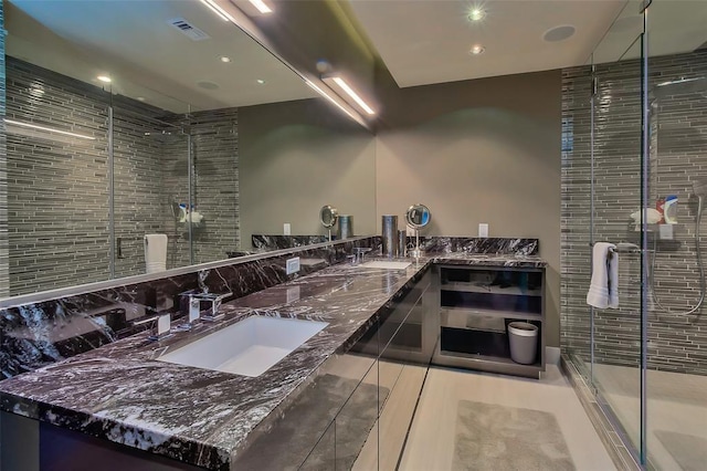 full bathroom with visible vents, a shower stall, backsplash, double vanity, and a sink