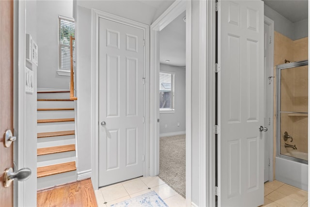 interior space featuring light tile patterned floors, stairway, baseboards, and light colored carpet