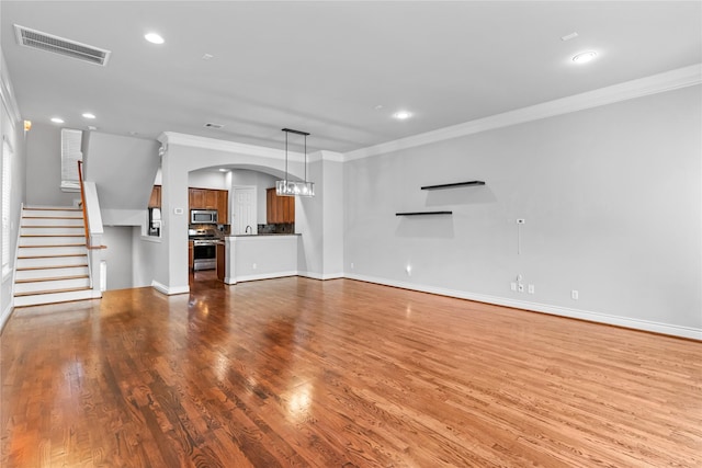 unfurnished living room with visible vents, crown molding, baseboards, stairs, and wood finished floors