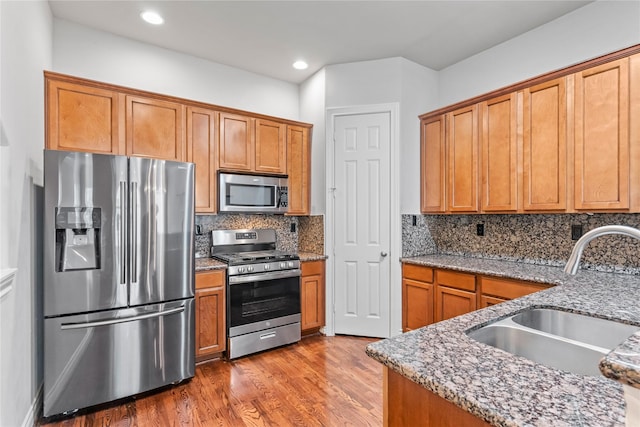 kitchen featuring light stone countertops, decorative backsplash, wood finished floors, stainless steel appliances, and a sink