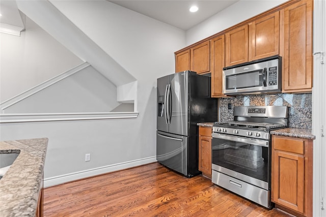 kitchen featuring tasteful backsplash, baseboards, appliances with stainless steel finishes, wood finished floors, and brown cabinetry