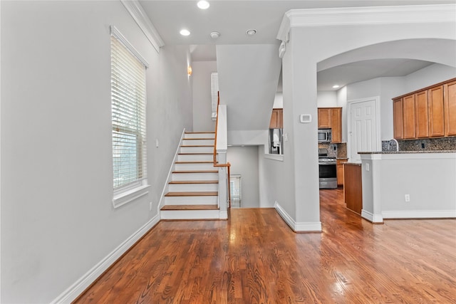 stairs with recessed lighting, wood finished floors, arched walkways, and baseboards