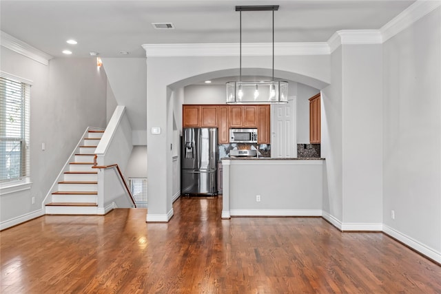 kitchen with stainless steel appliances, brown cabinets, dark countertops, and dark wood-style flooring