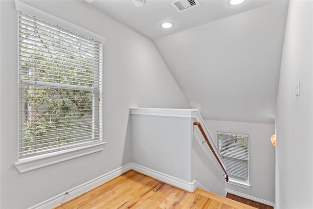 stairs featuring visible vents, plenty of natural light, lofted ceiling, and wood finished floors