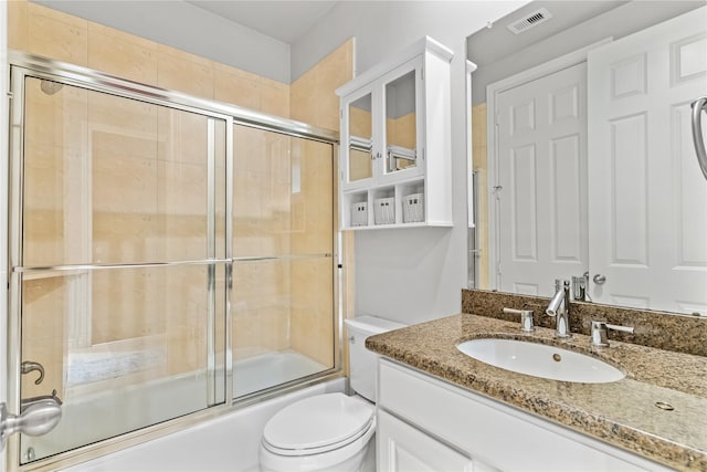 bathroom featuring visible vents, toilet, vanity, and shower / bath combination with glass door