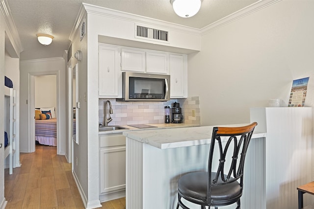 kitchen with crown molding, stainless steel microwave, a sink, and visible vents