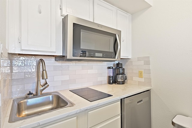 kitchen featuring stainless steel appliances, a sink, white cabinetry, light stone countertops, and tasteful backsplash