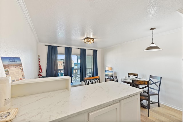 kitchen featuring white cabinets, ornamental molding, hanging light fixtures, a textured ceiling, and light wood-style floors