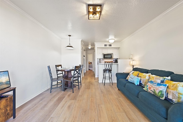 living area featuring ornamental molding, light wood-type flooring, visible vents, and a textured ceiling