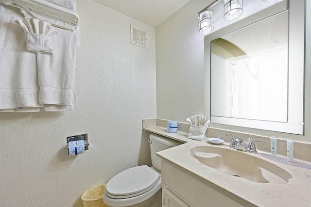 half bathroom featuring visible vents, a textured wall, vanity, and toilet