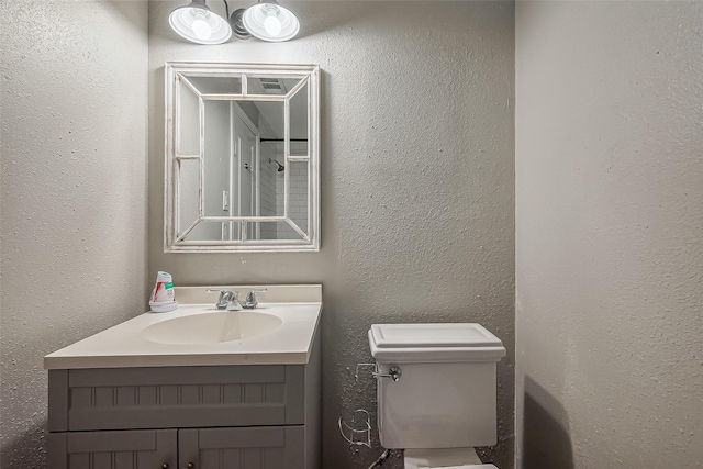 bathroom with a textured wall, vanity, and toilet