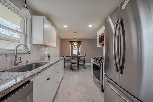 kitchen with light stone countertops, appliances with stainless steel finishes, white cabinets, and a sink