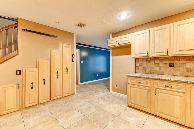 kitchen featuring light tile patterned floors, tasteful backsplash, visible vents, light stone countertops, and baseboards