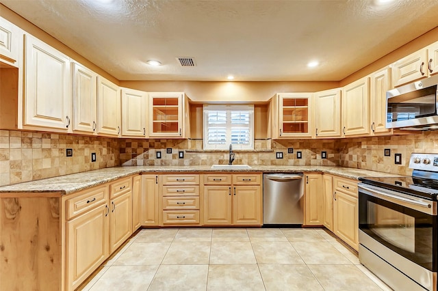 kitchen featuring light tile patterned floors, a sink, appliances with stainless steel finishes, decorative backsplash, and glass insert cabinets