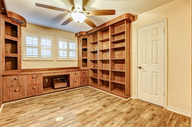 unfurnished office with a ceiling fan, built in study area, a textured ceiling, and wood finished floors