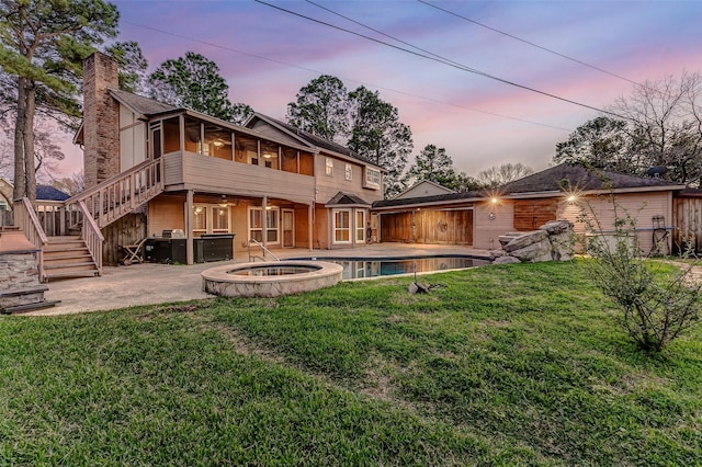 back of house featuring a sunroom, an in ground hot tub, stairs, a yard, and a patio area