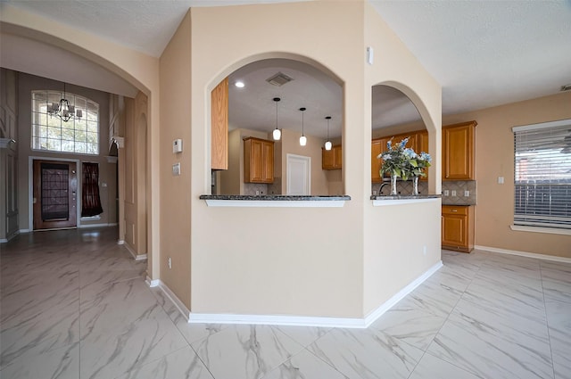 kitchen featuring baseboards, marble finish floor, backsplash, and brown cabinets