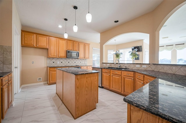 kitchen with dark stone countertops, arched walkways, a sink, appliances with stainless steel finishes, and marble finish floor