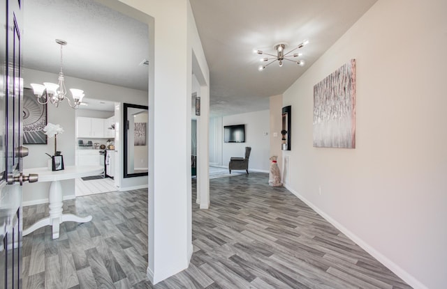 hallway featuring a chandelier, baseboards, and light wood-style floors