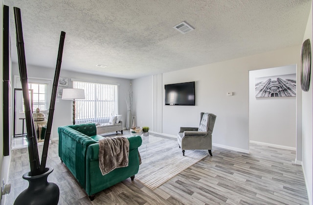 living room featuring light wood-type flooring, baseboards, visible vents, and a textured ceiling