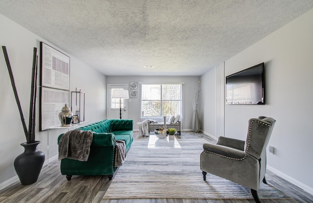 living room featuring a textured ceiling, baseboards, and wood finished floors