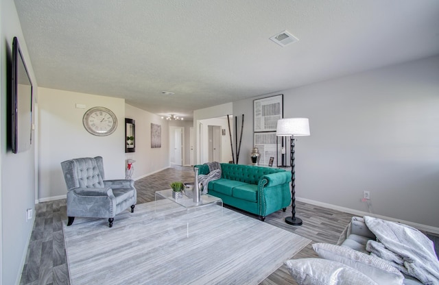 living area featuring visible vents, a textured ceiling, baseboards, and wood finished floors