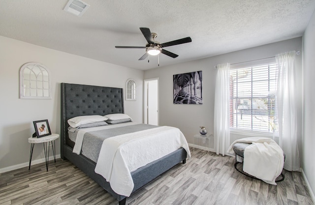 bedroom with ceiling fan, a textured ceiling, visible vents, and wood finished floors