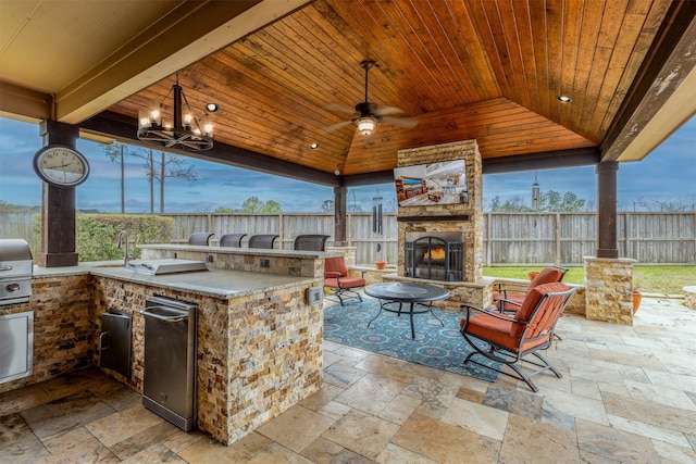 view of patio / terrace with fence, exterior kitchen, ceiling fan, an outdoor stone fireplace, and a gazebo